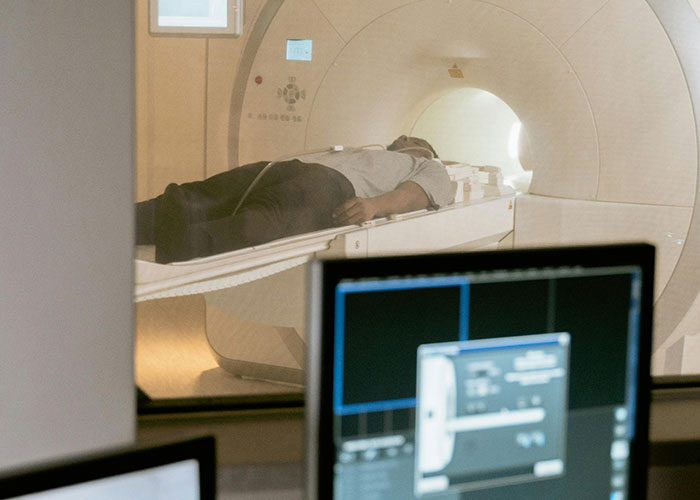 Person undergoing MRI scan in medical imaging room with computer monitors displaying diagnostic data nearby.