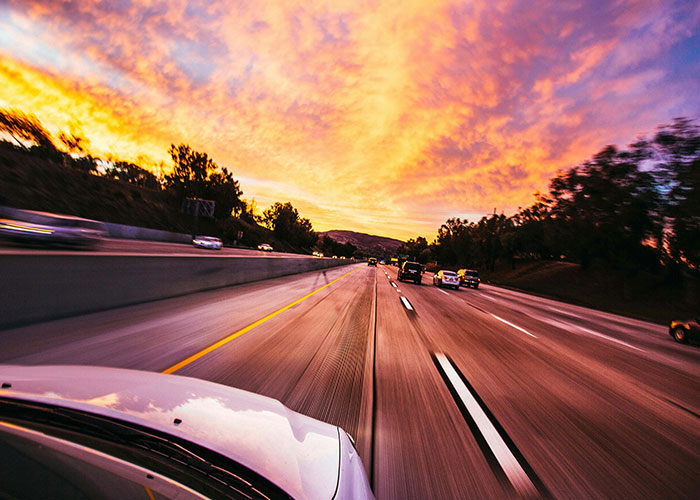 Car driving fast on highway at sunset, illustrating the illegal act of driving over the speed limit on open road.
