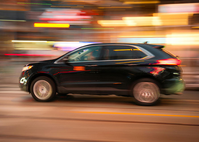 Black SUV speeding through city streets at night with blurred lights, illustrating wild and embarrassing drinking stories.