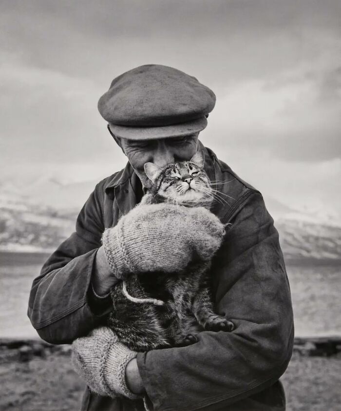 Man in vintage clothing holding a tabby cat outdoors, a classic vintage cat photo capturing timeless affection.