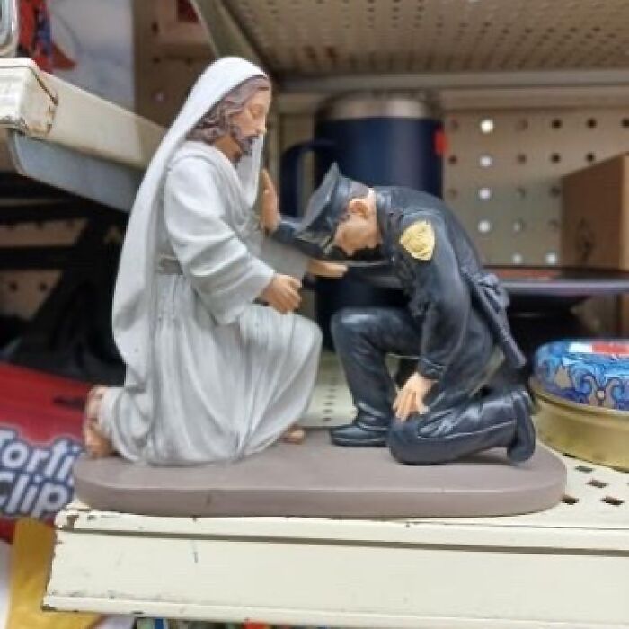 Figurine depicting a kneeling police officer being blessed by a kneeling Jesus, found at a thrift store among bizarre items.