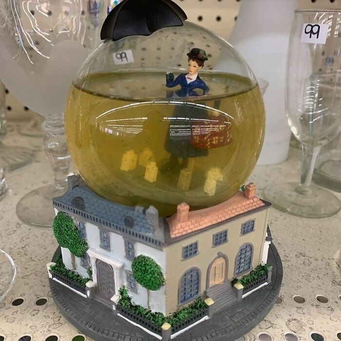 Bizarre thrift store find of a snow globe featuring a woman with an umbrella floating over a house model.