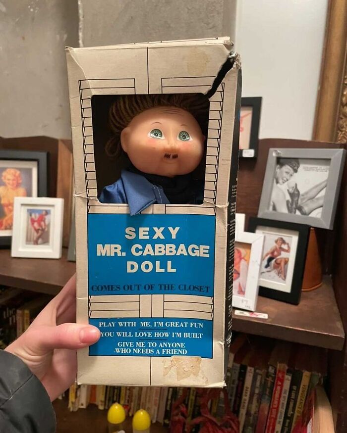 Vintage S**y Mr. Cabbage Doll in original box found among bizarre thrift store items on a wooden shelf background.