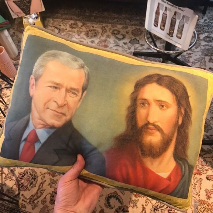 Hand holding a bizarre thrift store pillow featuring a unique print of two men, one in a suit and the other with long hair and beard.