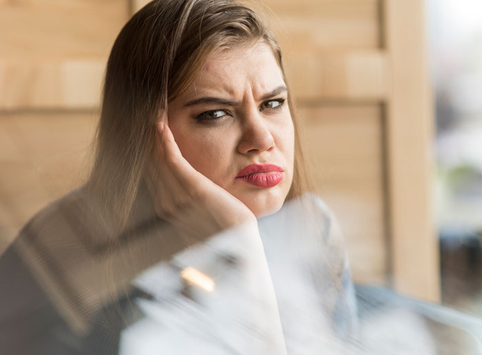 Woman with a frustrated expression resting her face on her hand, reflecting family demands and financial conflict.