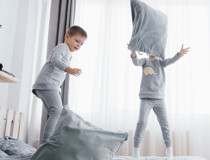 Two siblings in grey pajamas having a pillow fight on a bed, highlighting sibling moments and family dynamics. Two siblings in grey pajamas having a pillow fight on a bed, highlighting sibling moments and family dynamics.