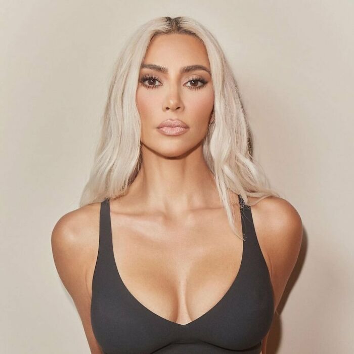 Kim Kardashian with platinum blonde hair, wearing a black top, promoting a viral beauty product in a studio setting.