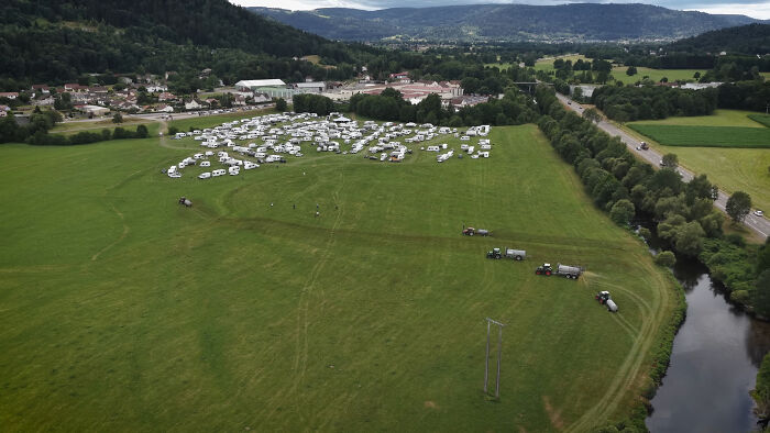 Aerial view of a large field with tractors spraying manure near campers and squatters during a viral farmer incident.