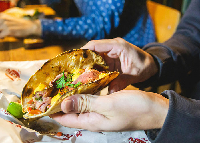 Person holding a taco at a table, illustrating wild and embarrassing drinking stories involving alcohol and poor decisions.