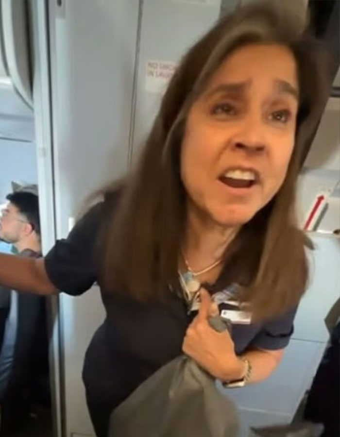 Flight attendant speaking firmly on plane near passenger seats during vaping incident and confrontation.