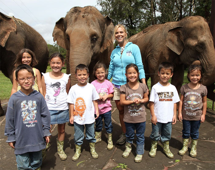 Group of children and a woman smiling in front of elephants, unrelated to locked up isolated zip tied or Collin's message.
