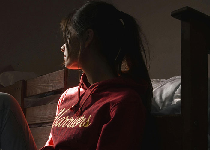 Young person in a dimly lit room, looking pensive, fitting the theme of someone tired of fun facts seeking horrifying ones.