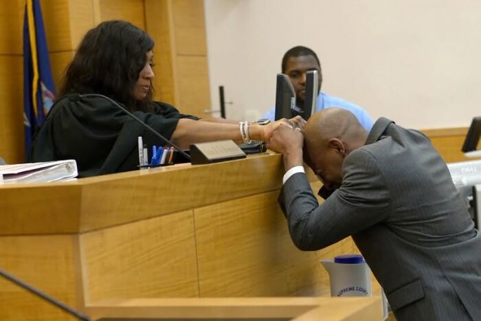 Man in courtroom leaning over bench holding hand of female judge in emotional moment, unsettling images from morbid knowledge group.