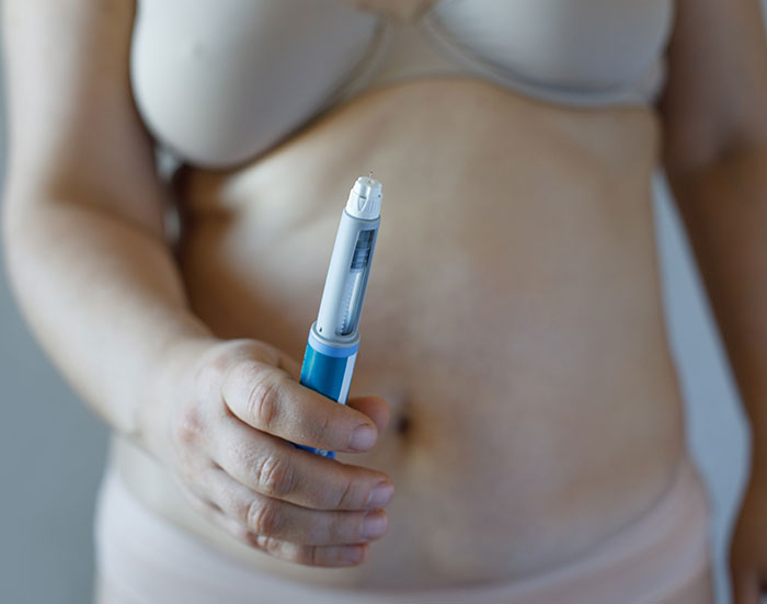 Person holding a blue and white injection pen in front of bare midsection, related to Ozempic vulva side effects.