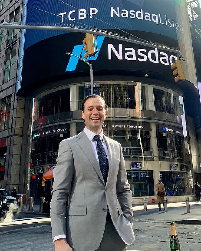 Man in gray suit standing smiling outside Nasdaq building, related to Uber driver brutal knockout and service dog incident.