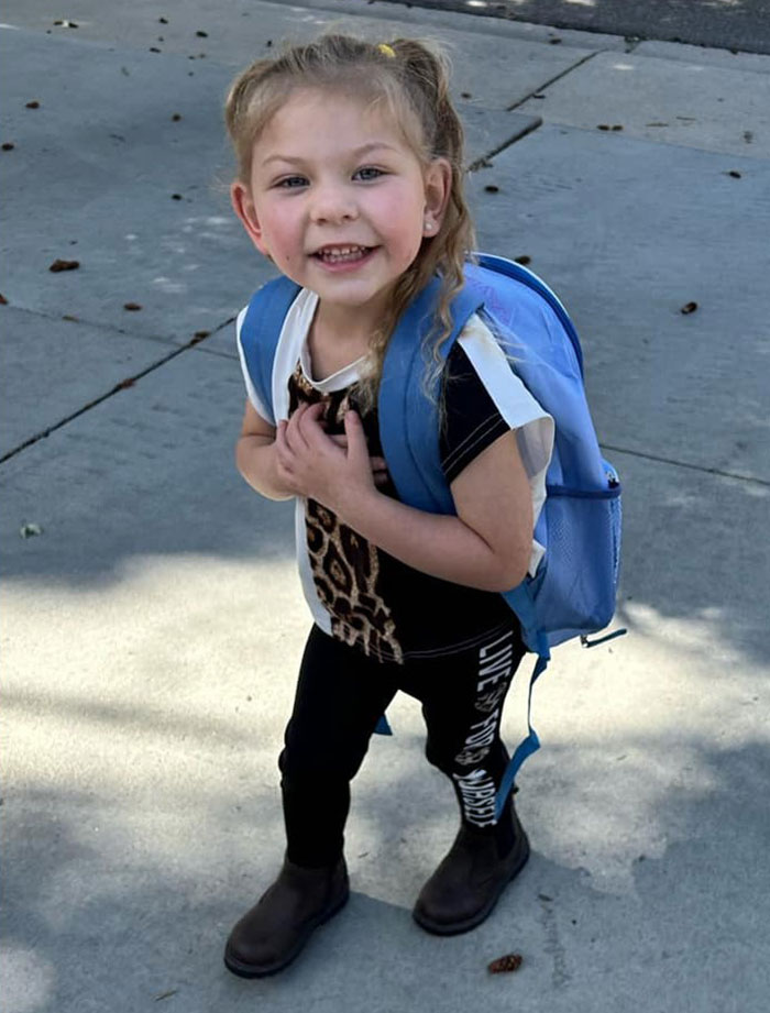 Young girl with a blue backpack smiling on sidewalk symbolizing family awarded after gravely disabled baby case.
