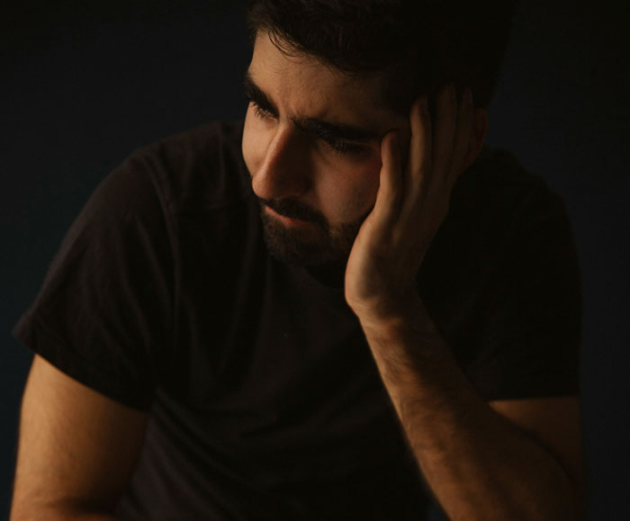Young man in a dark shirt looking down thoughtfully, reflecting on DNA test mixed results in a low-light setting.