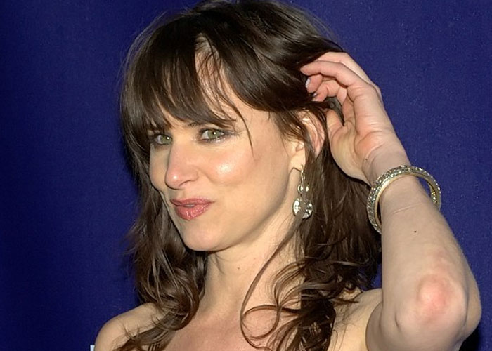 Woman with brown hair and earrings posing against a dark blue background in a total gentleman celebrity encounter.