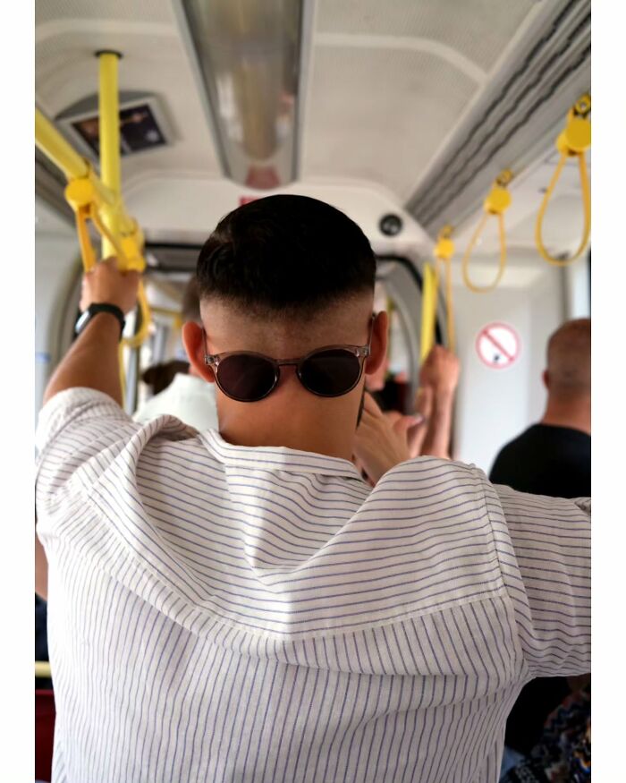 Man wearing sunglasses and striped shirt captured in an unseen, unposed moment on public transportation by street photographer.