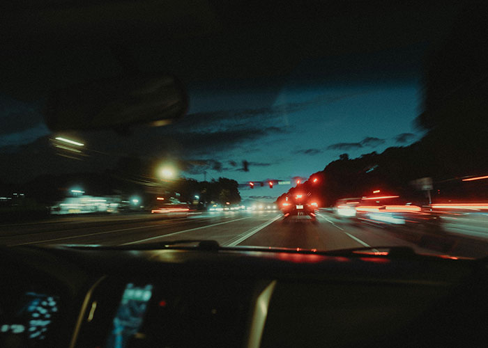 View from inside a car driving over the speed limit on a busy highway at night with blurred lights and traffic.