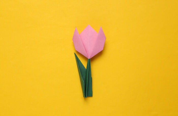 Origami pink flower with green leaves on a bright yellow background illustrating unhinged hacks to land job success.
