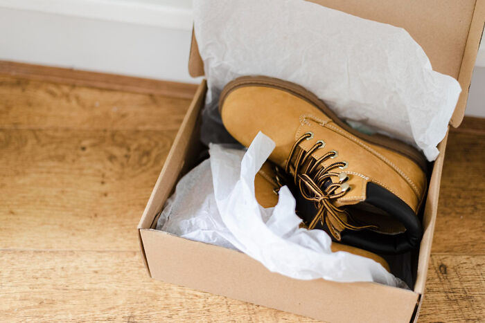 Brown leather boots in an open shoebox with white tissue paper on a wooden floor illustrating unhinged hacks done land job.