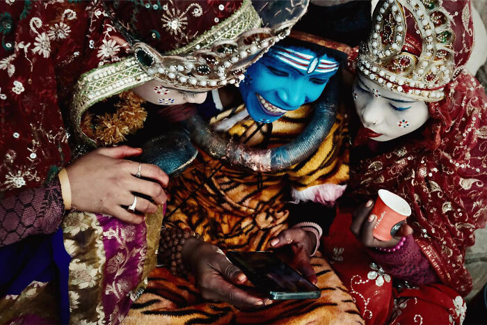 Three people in traditional Asian costumes and makeup sharing a candid moment looking at a phone together.