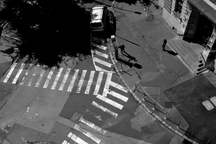 Black and white aerial view of street with pedestrians and a parked car, capturing unseen unposed moments on the streets.