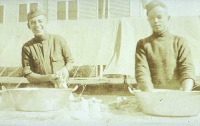 Two soldiers smiling while washing clothes in basins, showing daily life beyond the WWI trenches.