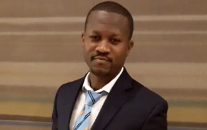 Man in a dark suit and striped tie standing indoors with a neutral expression, representing unsettling images from morbid knowledge group.