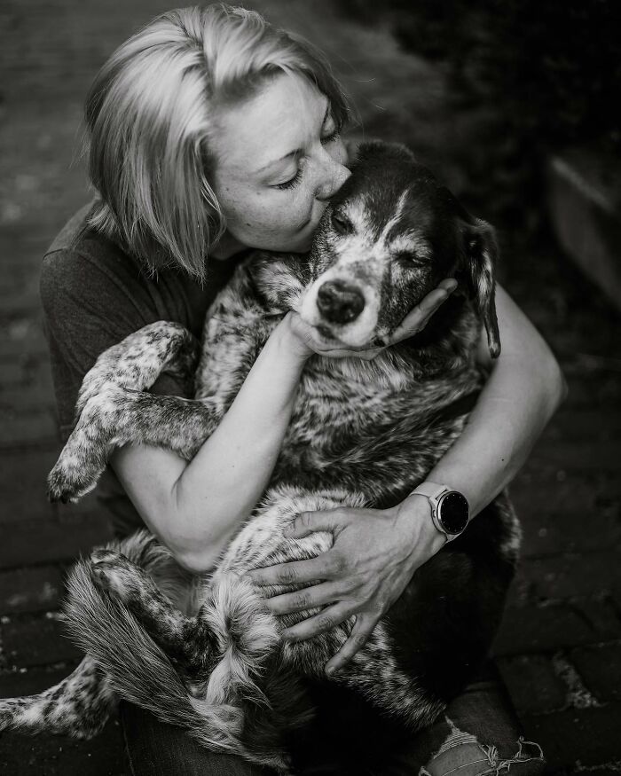 Woman tenderly holding and kissing her elderly dog, capturing touching final moments between pets and their humans in black and white.