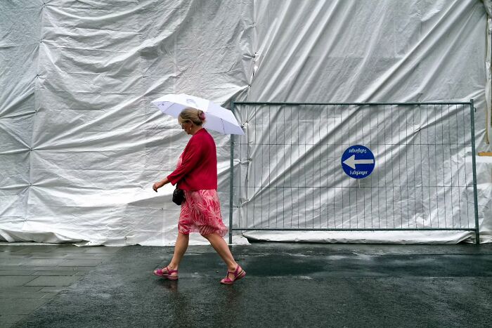 Woman walking on wet street with umbrella, captured in unseen unposed moments by street photographer.