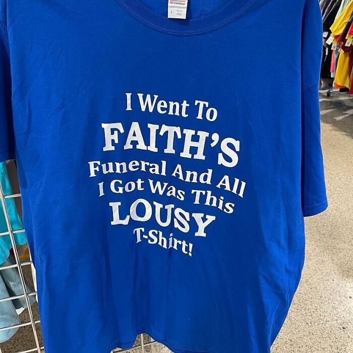 Blue thrift store T-shirt with humorous text about going to a funeral and getting a lousy shirt, displayed in a store.
