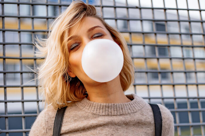 Young woman blowing a bubblegum bubble outdoors, illustrating smooth pickup lines in a casual urban setting.