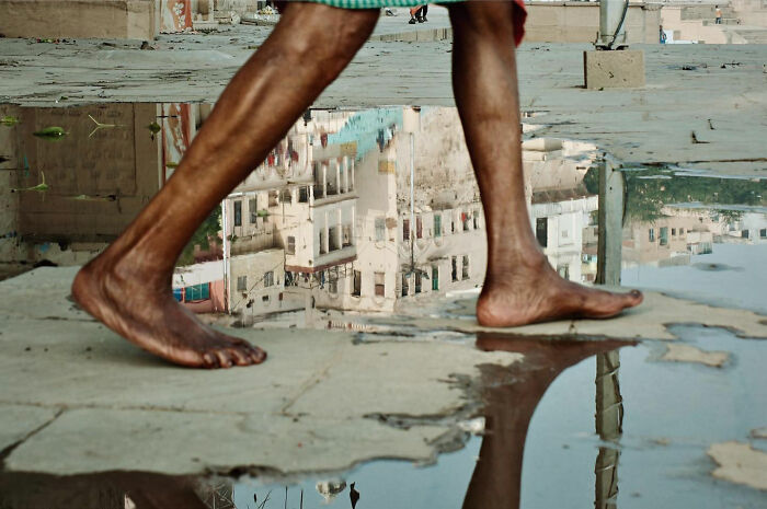 Bare feet walking near a puddle reflecting urban buildings in a candid everyday moment from Asia by photographer Gil Kreslavsky.