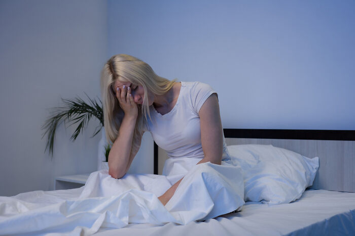 Woman sitting on bed at night looking distressed, illustrating scary sounds heard by people in chilling true stories.