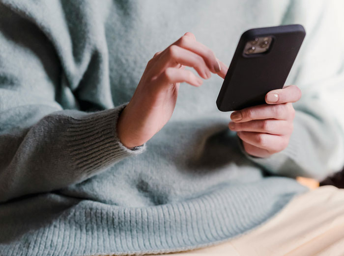 Woman in a gray sweater holding and interacting with a smartphone, reflecting on separation and divorce differences.