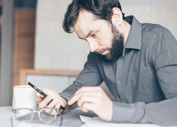 Man with a beard wearing a gray shirt looking worried while using a phone, symbolizing fears about pregnancy and family conflict. Man with a beard wearing a gray shirt looking worried while using a phone, symbolizing fears about pregnancy and family conflict.