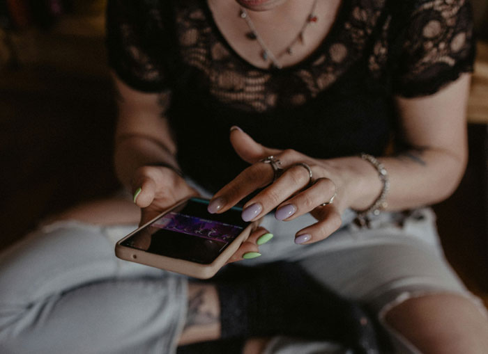Woman with colorful nails using smartphone, representing a man giving pregnant girlfriend an ultimatum over insecurities.