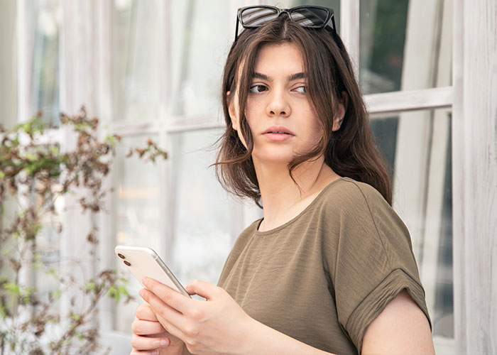 Young woman holding smartphone outdoors, showing petty revenge on entitled dog owner with a clever button press.