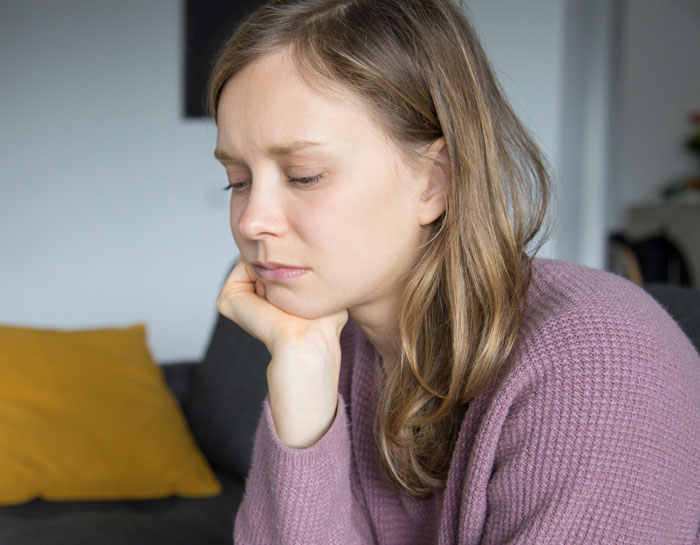 Sad woman in a purple sweater sitting indoors, reflecting on family demands and strained relationships over money.