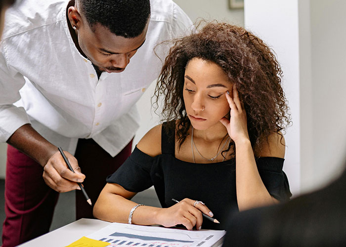 Intern and coworker discussing paperwork in an office setting, highlighting intern ends up hospitalized after cupcakes incident.