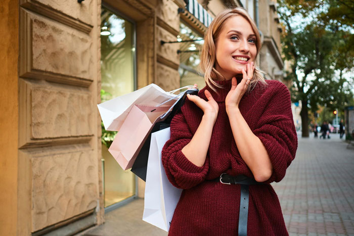 Woman carrying shopping bags outdoors, smiling and wearing a burgundy sweater, representing wife and job allowance concept. Woman carrying shopping bags outdoors, smiling and wearing a burgundy sweater, representing wife and job allowance concept.