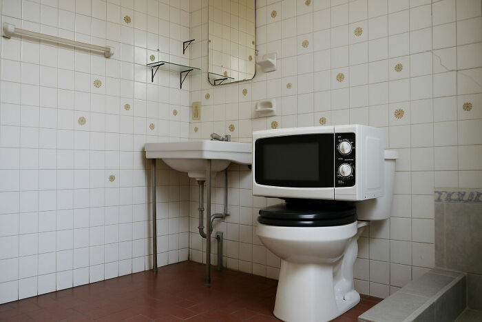 Microwave placed on a toilet in a bathroom with tiled walls, showcasing a weird thing seen in someone else’s home. - 15