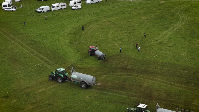 Aerial view of a farmer spraying manure with a tractor near squatters&rsquo; caravans on a large grassy field.