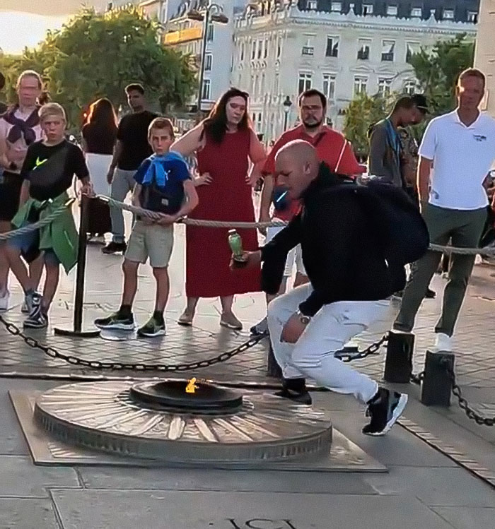 Man lighting cigarette on Tomb of Unknown Soldier flame while bystanders watch, facing arrest and deportation risks. - 4