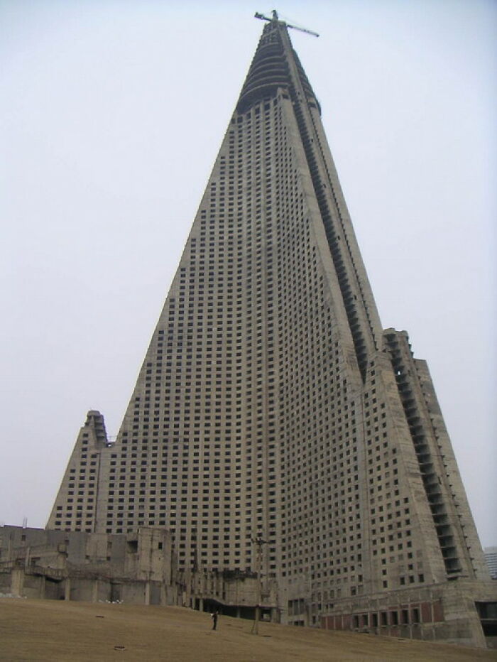 Abandoned pyramid-shaped building with many windows and a crane on top in a desolate area, an example of abandoned places.