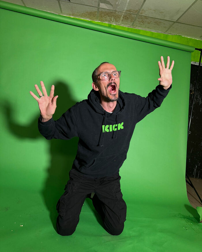 Man in black hoodie with glasses, kneeling and expressing shock in front of a green screen, representing famous streamer. Man in black hoodie with glasses, kneeling and expressing shock in front of a green screen, representing famous streamer.