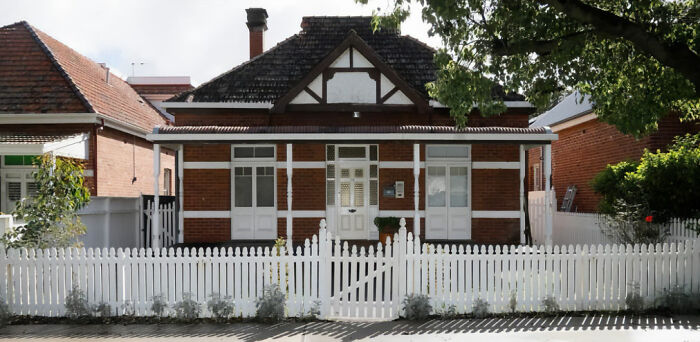 Abandoned million-dollar house with white picket fence and brick exterior, linked to couple accused of squatting and renovating.