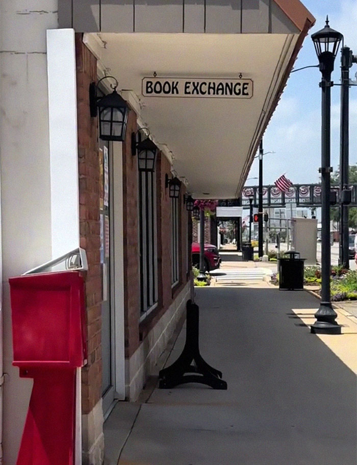 Sidewalk view of a building with a book exchange sign and street lamps on a sunny day in a small town. Sidewalk view of a building with a book exchange sign and street lamps on a sunny day in a small town.